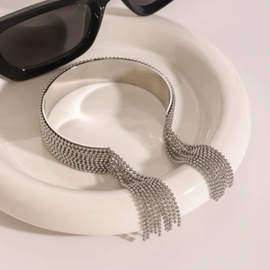 Polished stainless steel cuff bracelet with long bead tassels on a white ceramic plate