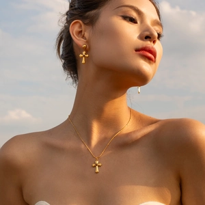 Gros plan du collier et boucles d'oreilles croix dorés avec texture martelée