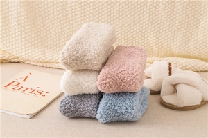 Nahaufnahme flauschiger Wintersocken in Beige, Rosa und Grau auf einer Strickdecke