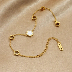 Goldenes Edelstahl-Armband mit weißen Perlmutt-Blumen auf goldenem Seidenstoff drapiert