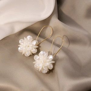 Detail of elegant white long flower petal earrings with golden hooks on silk background