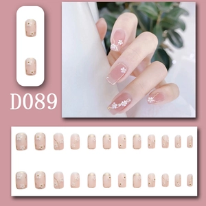Detail of pink press-on nails with white flower patterns and golden glitter accents