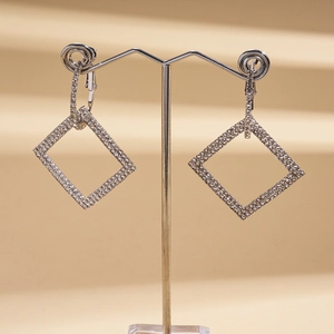 Macro view of geometric silver earrings with inlaid crystals on a beige pedestal