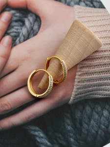 Detailed view of gold-plated hoop earrings with cubic zirconia on a wooden display stand
