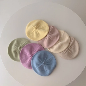 Pastel knit berets for babies in cream, pink, and khaki on a white table