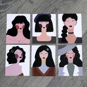 Flat lay of six cartoon female portrait jewelry display cards on a gray wood background