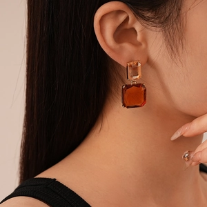 Gros plan de boucles d'oreilles carrées en cristal ambré portées par un mannequin chic