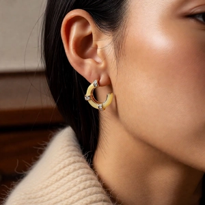 Macro side view of a model wearing gold bamboo-shaped C-hoop earrings with small crystals
