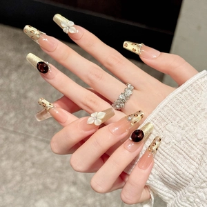 Detail of luxury press-on nails with white 3D flowers, amber leopard print, and red gems