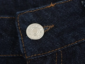 Détail macro de la taille en denim bleu foncé avec bouton argenté et coutures contrastées