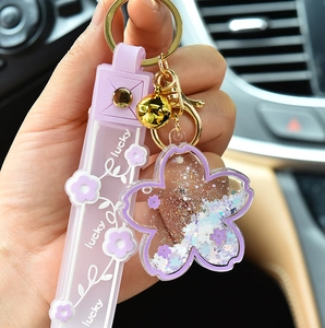 Detail view of purple Sakura quicksand keychain with lucky strap and golden bell.
