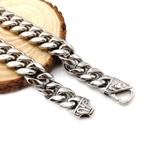 Polished silver stainless steel Cuban link bracelet with ornate engraved vine clasp on wood