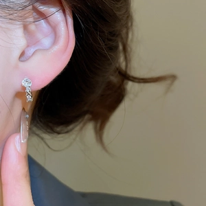 Close-up of silver-plated U-shaped earrings with zircon stones on a model's ear