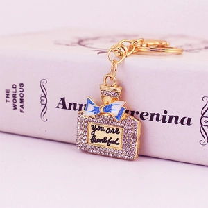 Goldener Parfümflaschen Schlüsselanhänger mit Strass und blauer Schleife auf Buch