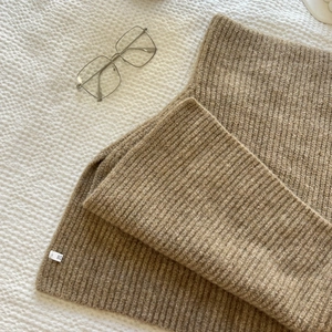 Close-up of brown ribbed knit sweater scarf with a small white label on white fabric