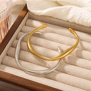 Irregular stainless steel open bangle in gold and silver finish on a display tray