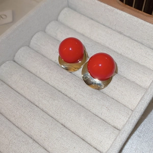 Macro shot of red round beads on textured golden metal bases of stylish stud earrings