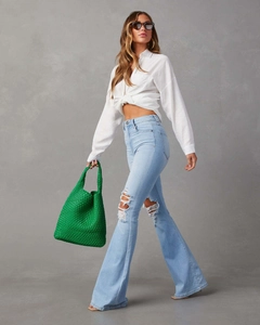 Détail d'un jean évasé à taille haute avec déchirures, denim bleu clair et genou usé