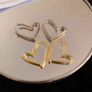 Minimalist gold and silver hollow heart hoop earrings reflected on a round mirror surface