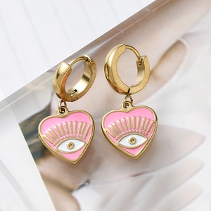 Close-up of golden hoop earrings with pink heart charms and enamel evil eye design