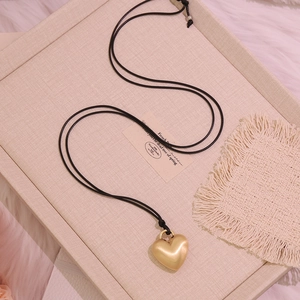 Detail of a matte gold heart-shaped pendant on a minimalist long black cord necklace