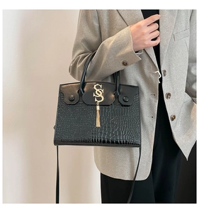 Detail of black crocodile pattern handbag with gold S-logo and tassel on grey blazer