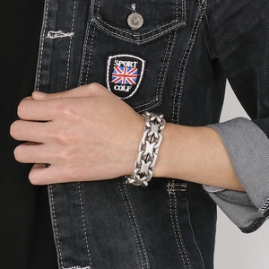 Close-up of a silver stainless steel curb chain bracelet worn by a person in a denim jacket