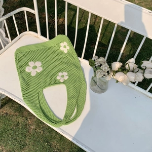 Nahaufnahme einer grünen Häkeltasche mit weißen Blumen auf einer Gartenbank