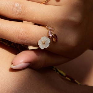 Elegant gold flower ring with pearl shell and pink gems worn on model's finger
