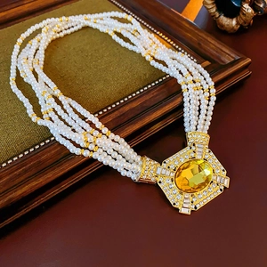 Dettaglio macro di collana di perle a più strati con grande pendente d'oro e gemma gialla
