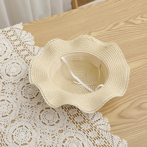 Dettaglio cappello di paglia beige con tesa ondulata e cinturino interno regolabile