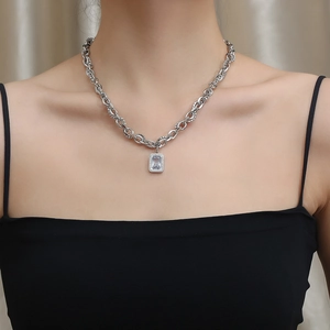 Close-up of a silver cuban chain necklace with a rectangular zircon pendant on a model