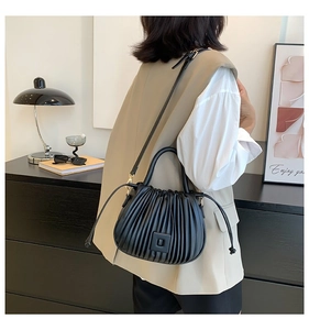 Detailed view of black pleated texture handbag with leather patch and slim shoulder strap
