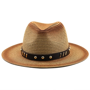 Close-up of woven straw fedora hat featuring a leather band with golden rivets