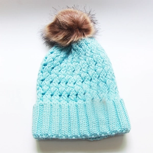 Detailed view of light blue cable knit beanie with fluffy brown faux fur pom pom