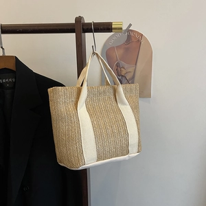 Detail of a beige straw handbag with white canvas handles hanging on a wooden hanger