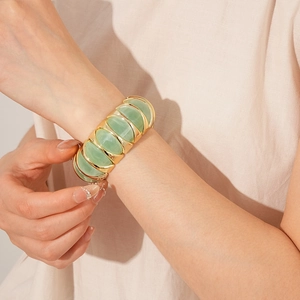 Close-up of a wide golden bangle with green resin inlay worn by a model in warm light