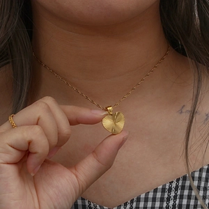 Close-up of golden heart pendant necklace with fine radial texture on twisted rope chain