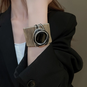 Detail of wide metal cuff bracelet featuring gold wires and black circular center ornament