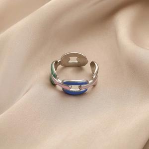 Détail d'une bague chaîne argentée avec émail coloré posée sur un tissu en soie beige