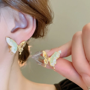 Gros plan de boucles d'oreilles papillon dorées avec ailes en nacre verte sur mannequin