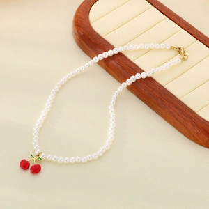 Macro view of white pearls and red resin cherry pendant on a wooden display stand
