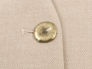 Close-up of vintage gold button on textured beige fabric of a women's blazer jacket