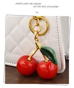 Detail of red cherry resin pendant with gold metal stem and glittery green leaves