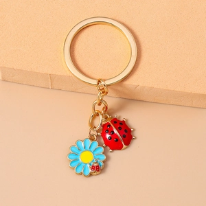Detail of keychain with red enamel ladybug and blue daisy charms on a gold ring