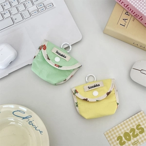 Detail of canvas earbud case with floral trim, snap button, and carabiner in lifestyle setting