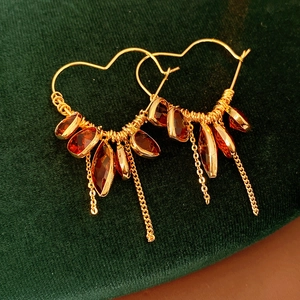 Detail of 18K gold heart earrings with red gemstones and elegant metal tassels