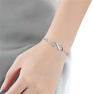 Detailed close-up of a silver infinity charm bracelet worn on a woman's wrist