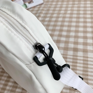 Détail du sac bandoulière en toile blanche montrant la fermeture éclair et la sangle