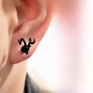 Detail view of a black matte ram head stud earring with textured horns on a model's ear